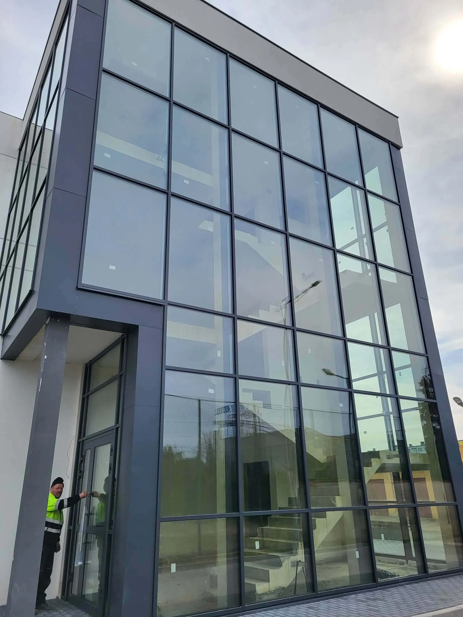 Fasada aluminiowa budynku biurowego, monter w kamizelce odblaskowej przy drzwiach wejściowych
